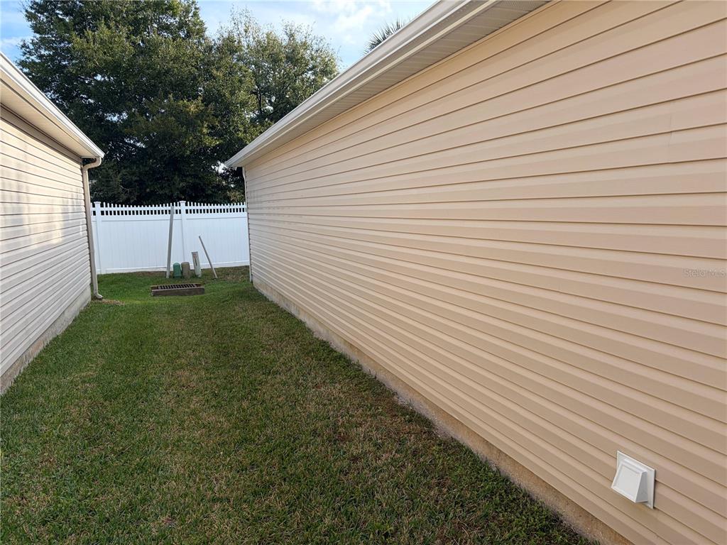 A narrow grassy side yard sits between two houses with beige vinyl siding — 675 KENDALL COURT, THE VILLAGES, FL