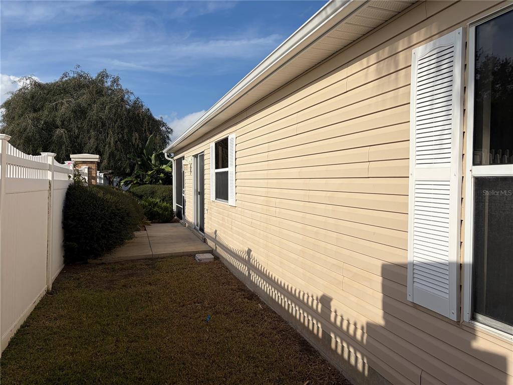 The side exterior of a house features beige vinyl siding, white shutters, and a walkway — 675 KENDALL COURT, THE VILLAGES, FL