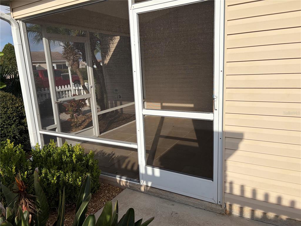 A screened-in porch with a white frame door and beige vinyl siding on the exterior — 675 KENDALL COURT, THE VILLAGES, FL