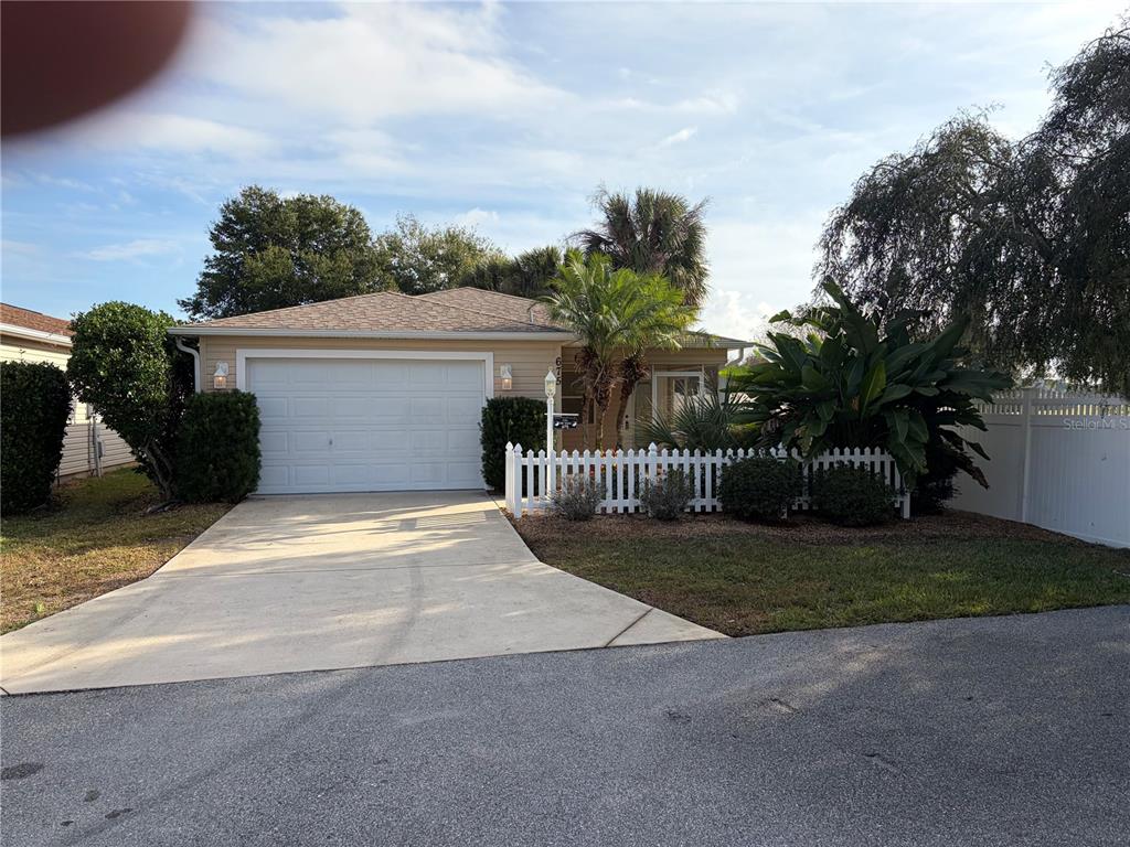 A single-story house with a white garage door, a concrete driveway, and a white picket fence — 675 KENDALL COURT, THE VILLAGES, FL