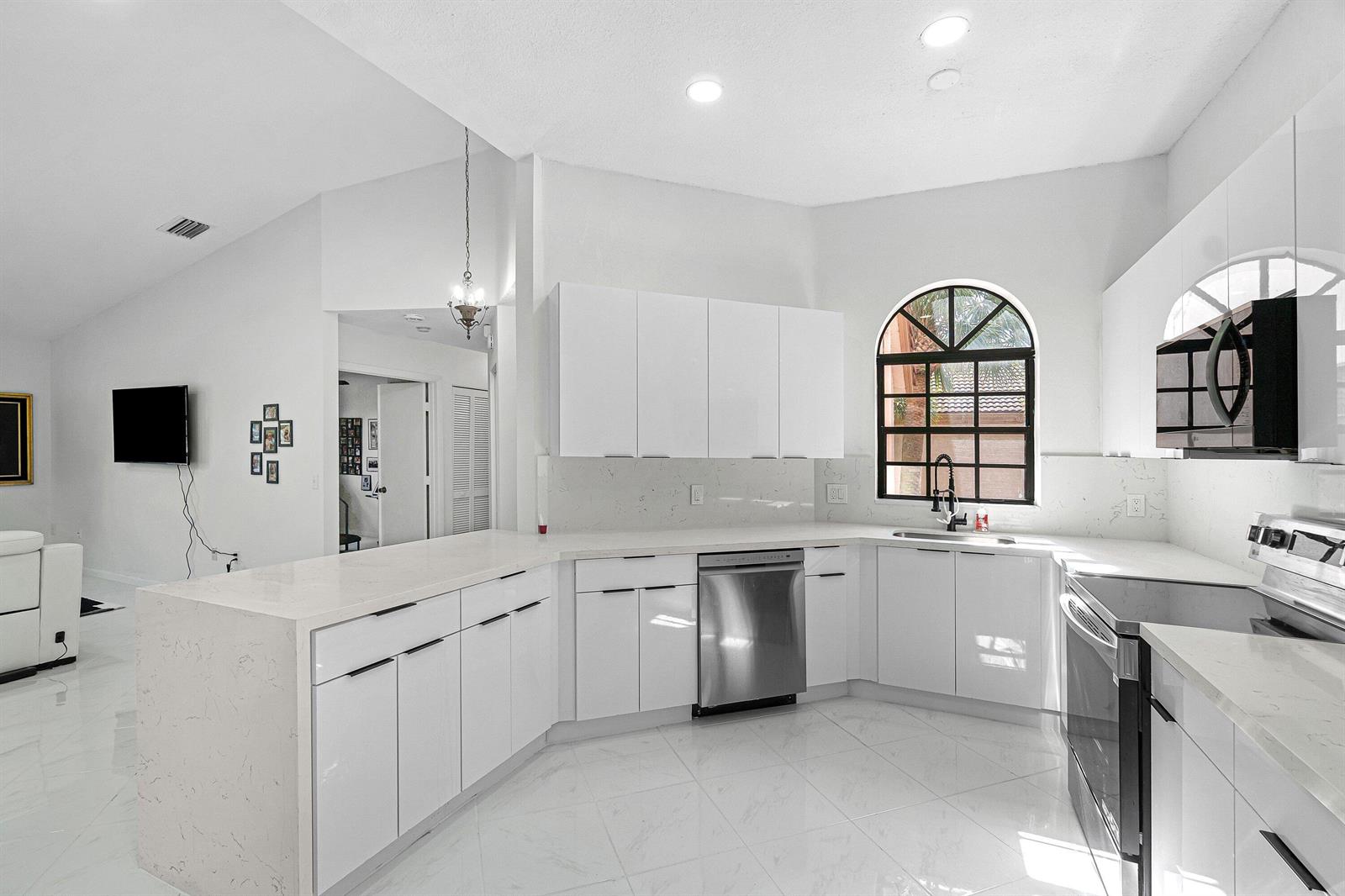 A modern white kitchen features glossy cabinets, quartz countertops, stainless steel appliances, and tile flooring — 5171 Europa Drive # G, Boynton Beach FL 33437, BOYNTON BEACH, FL