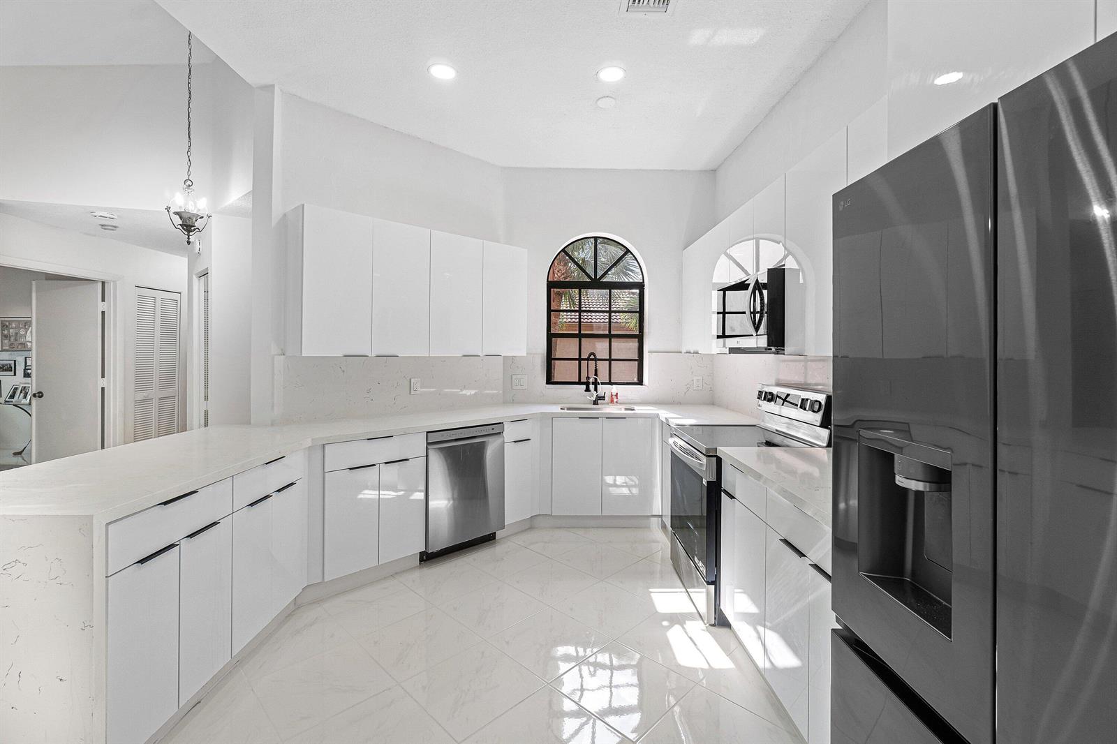A modern white kitchen features stainless steel appliances, quartz countertops, and a large arched window — 5171 Europa Drive # G, Boynton Beach FL 33437, BOYNTON BEACH, FL
