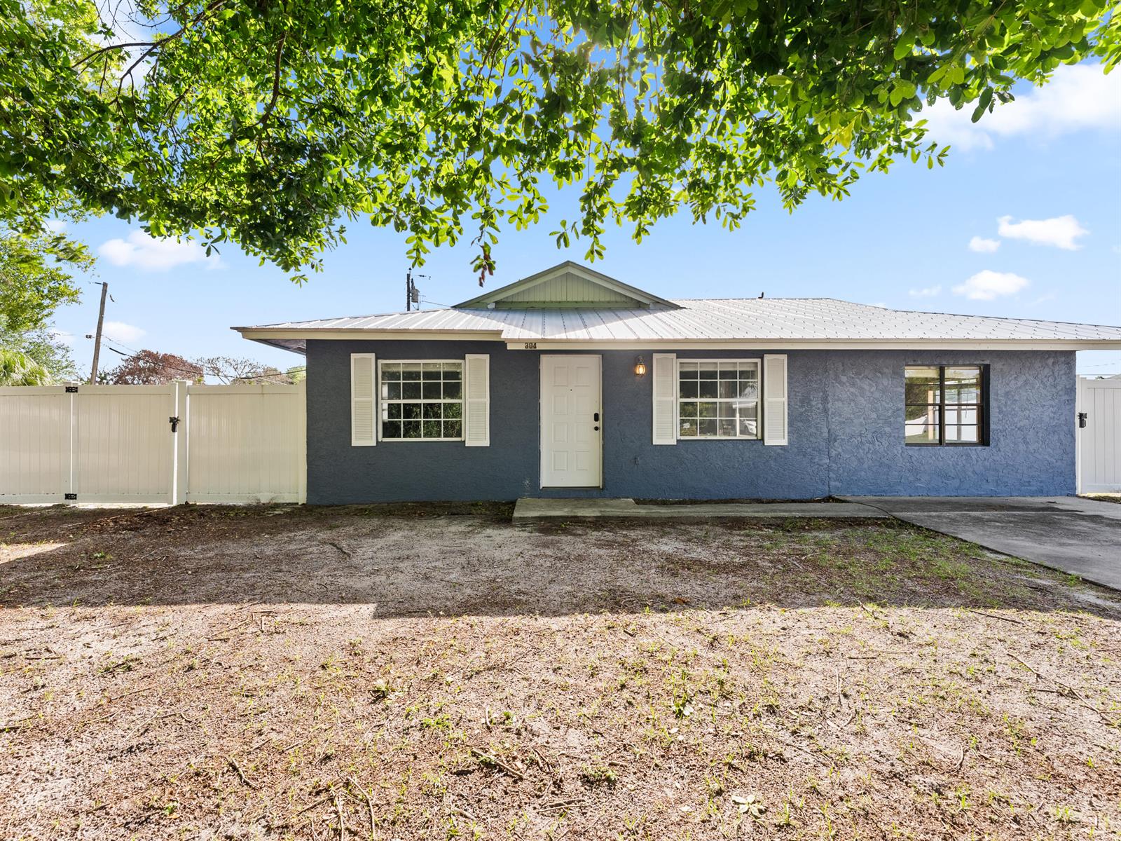 A single-story blue house with a metal roof and white shutters stands behind a yard — 304 8th Avenue SW, Vero Beach FL 32962, VERO BEACH, FL