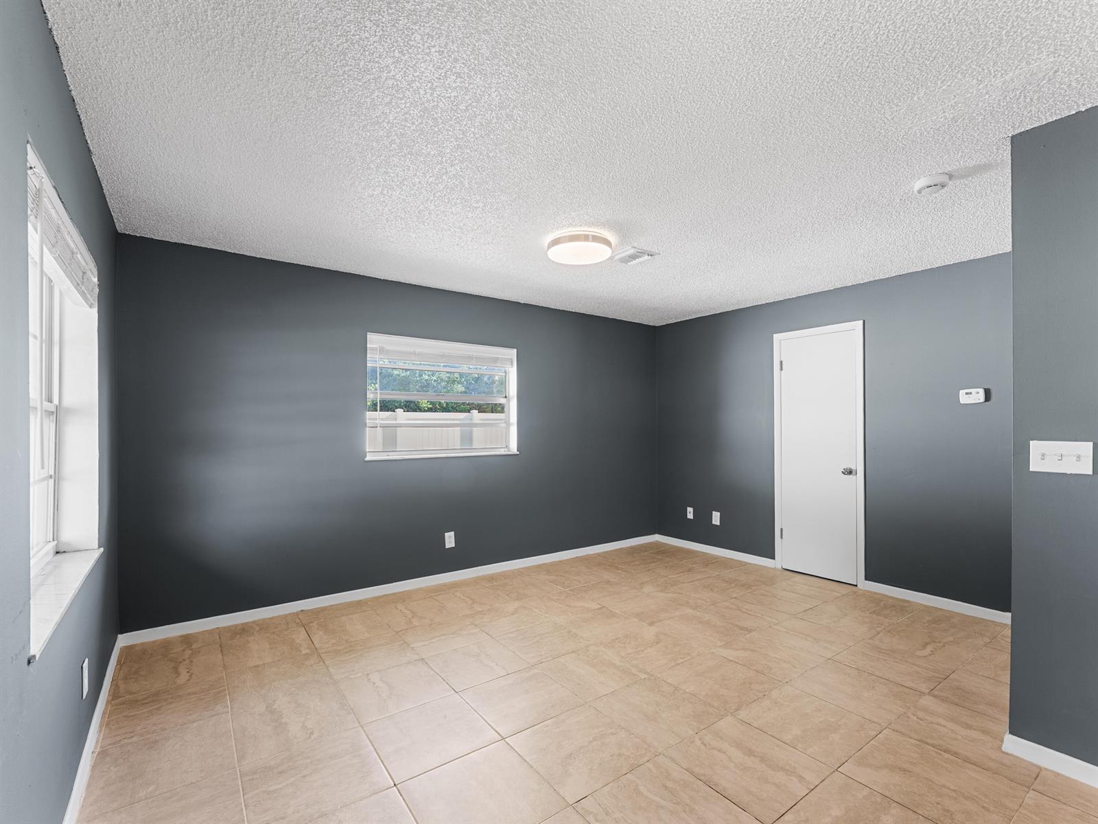 An empty room with dark gray walls, beige tile flooring, and a white popcorn ceiling — 304 8th Avenue SW, Vero Beach FL 32962, VERO BEACH, FL