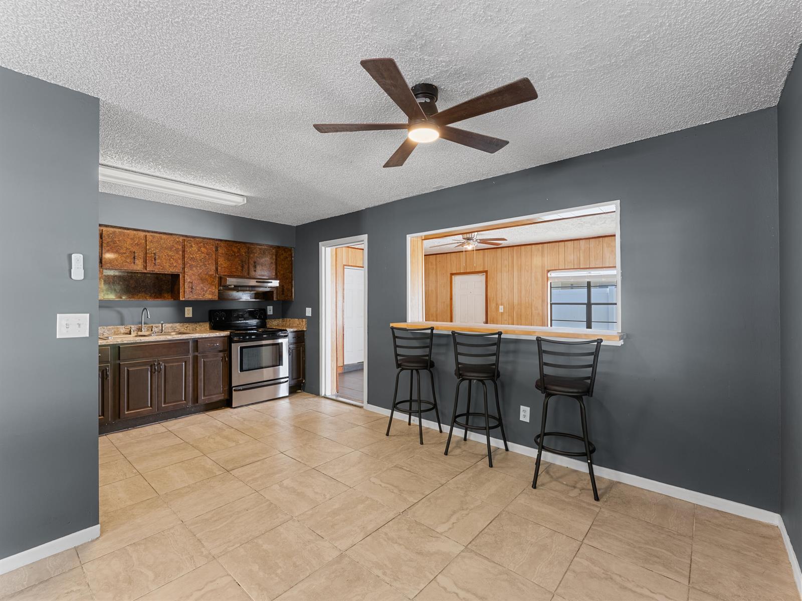A kitchen with dark cabinets, tile flooring, and a breakfast bar opening to another room — 304 8th Avenue SW, Vero Beach FL 32962, VERO BEACH, FL