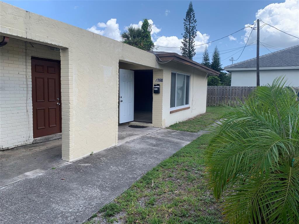 A beige, single-story building features a brown door, an open white door, and a walkway — LAUDERHILL, FL