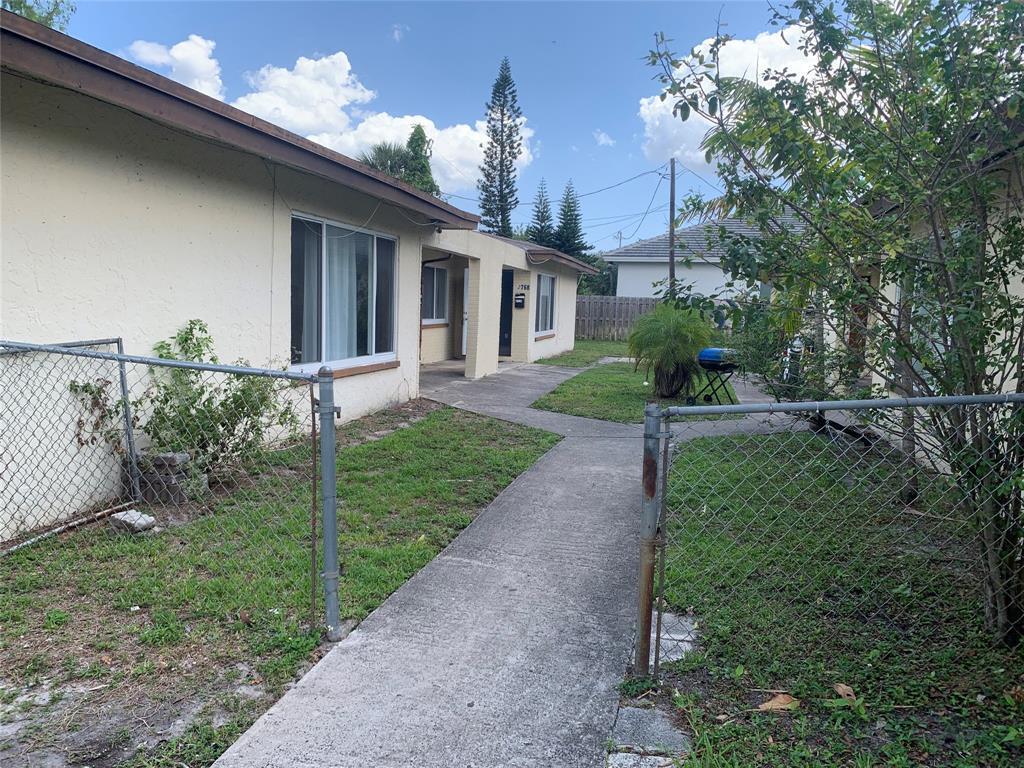 A concrete walkway leads to the entrance of a single-story stucco building with chain-link fencing — LAUDERHILL, FL