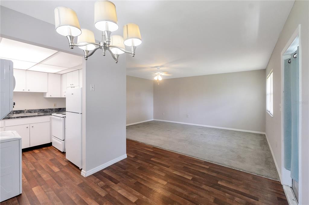 A kitchen with white cabinets and wood-look flooring opens into a carpeted living area — 201 KINGS BOULEVARD UNIT 5, SUN CITY CENTER, FL