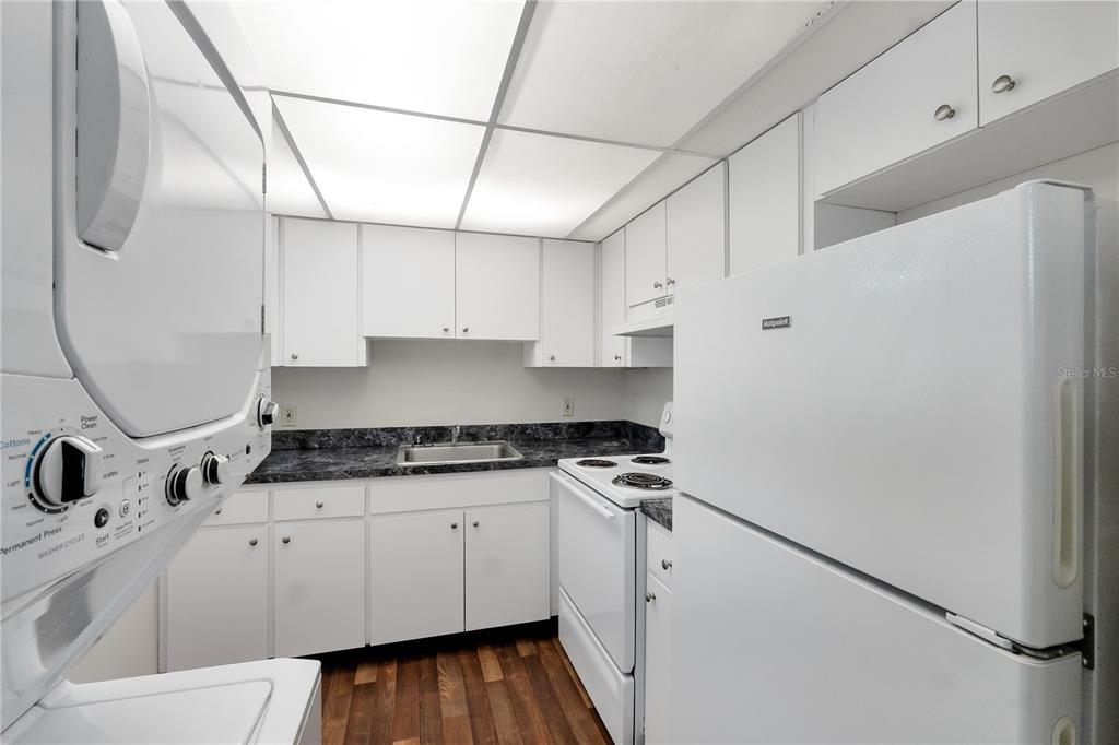 A small kitchen features white cabinets, white appliances, a dark countertop, and wood-look flooring — 201 KINGS BOULEVARD UNIT 5, SUN CITY CENTER, FL