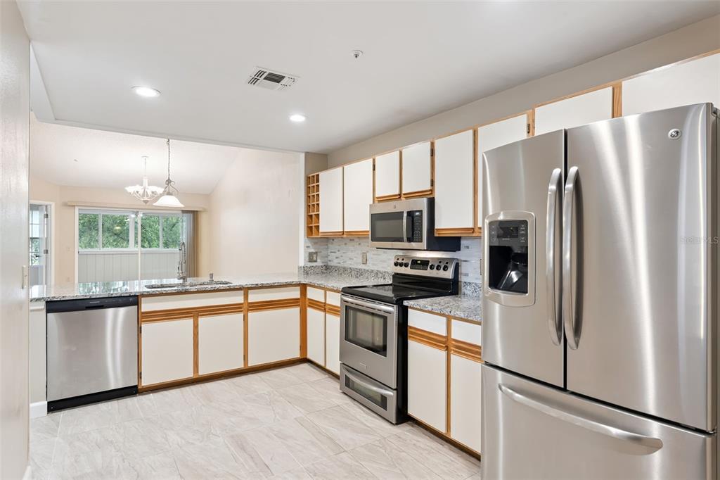 A kitchen features white cabinets with wood trim, stainless steel appliances, and granite countertops — 683 POST OAK CIRCLE UNIT 105, ALTAMONTE SPRINGS, FL