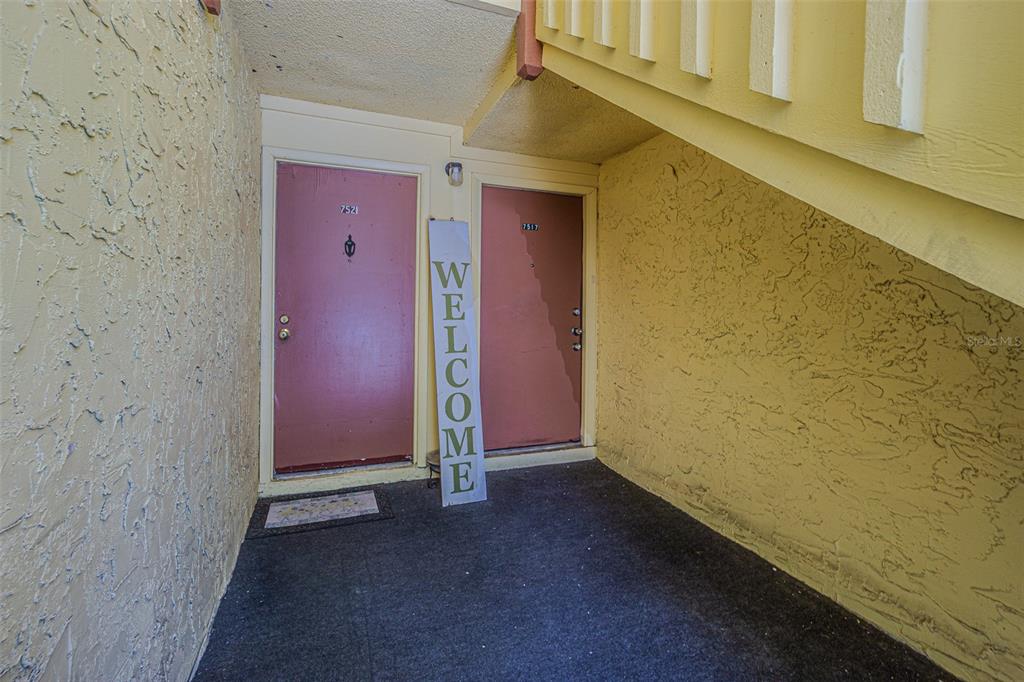 An exterior view of two apartment doors with a welcome sign on a concrete landing — 7517 ABONADO ROAD UNIT 7517, TAMPA, FL