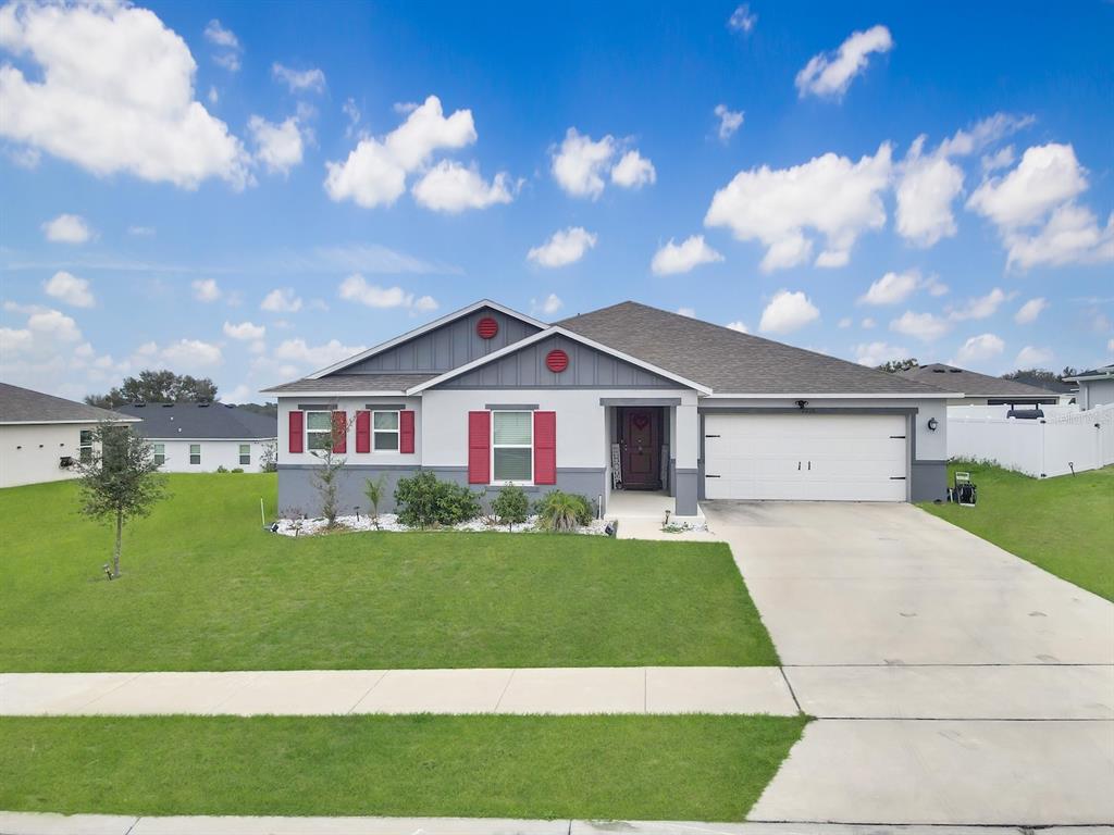 A single-story house with a white garage, gray siding, and red shutters under a blue sky — 2220 GLADIOLUS LANE, MASCOTTE, FL
