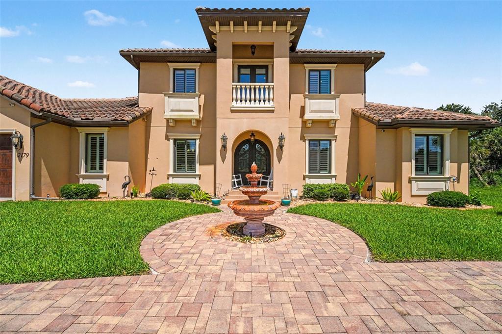 A two-story stucco house with a tiled roof, arched entryway, and a circular stone fountain — 2179 ARNOLD PALMER DRIVE, TITUSVILLE, FL