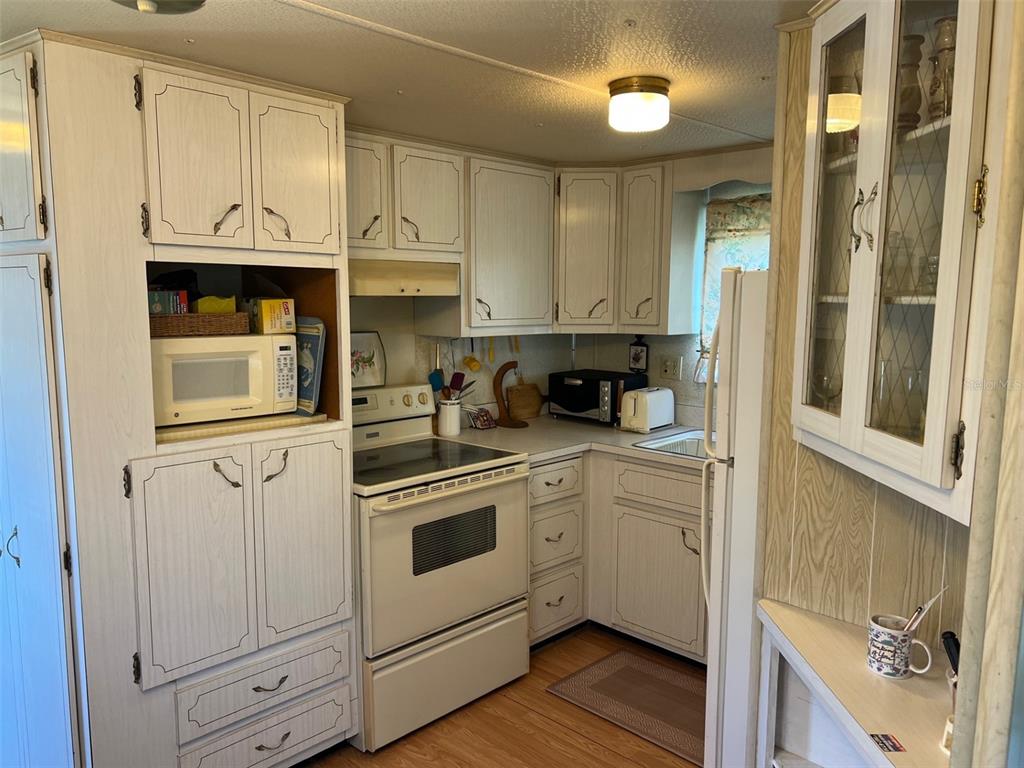 A kitchen features white cabinets, a white stove, a built-in microwave, and wood-look flooring — 12674 SEMINOLE BOULEVARD UNIT M1, LARGO, FL