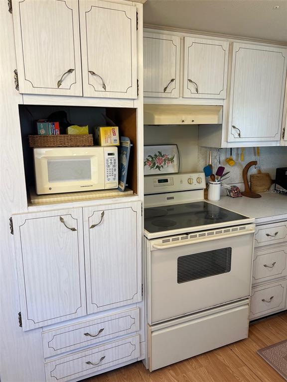 A kitchen features white wood-grain cabinets, a microwave in an open shelf, and a white stove — 12674 SEMINOLE BOULEVARD UNIT M1, LARGO, FL
