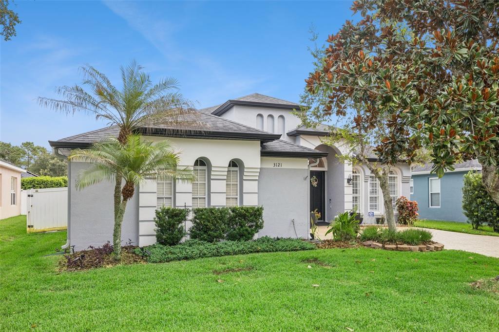 A single-story house with a gray stucco exterior, arched windows, and a palm tree — 3121 JUNEBERRY TERRACE, OVIEDO, FL