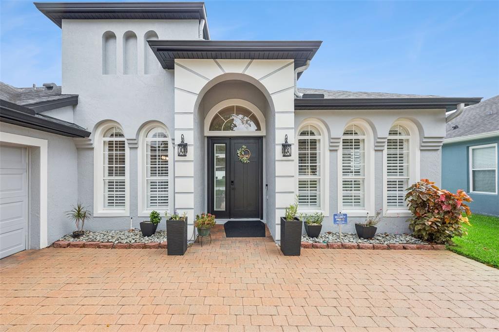 A gray house exterior features a paved driveway, arched windows, and a central arched entryway — 3121 JUNEBERRY TERRACE, OVIEDO, FL