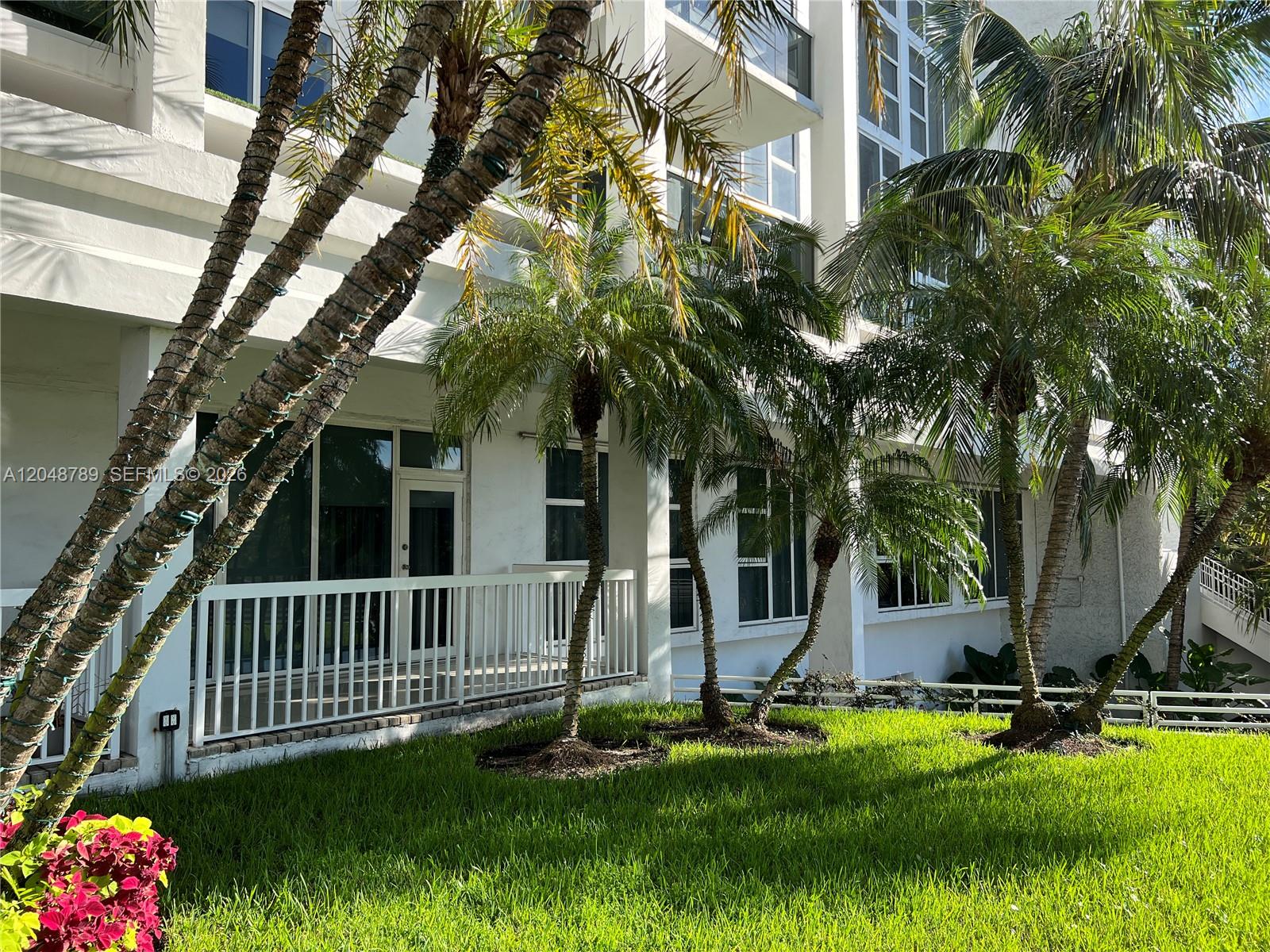 The exterior of a multi-story building features a white balcony, palm trees, and green grass — 10275 Collins Ave # 112, Bal Harbour FL 33154, BAL HARBOUR, FL
