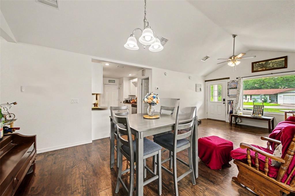 A dining area with a wooden table, chairs, and wood-look flooring opens into a kitchen — 17050 SE 60TH STREET, OCKLAWAHA, FL
