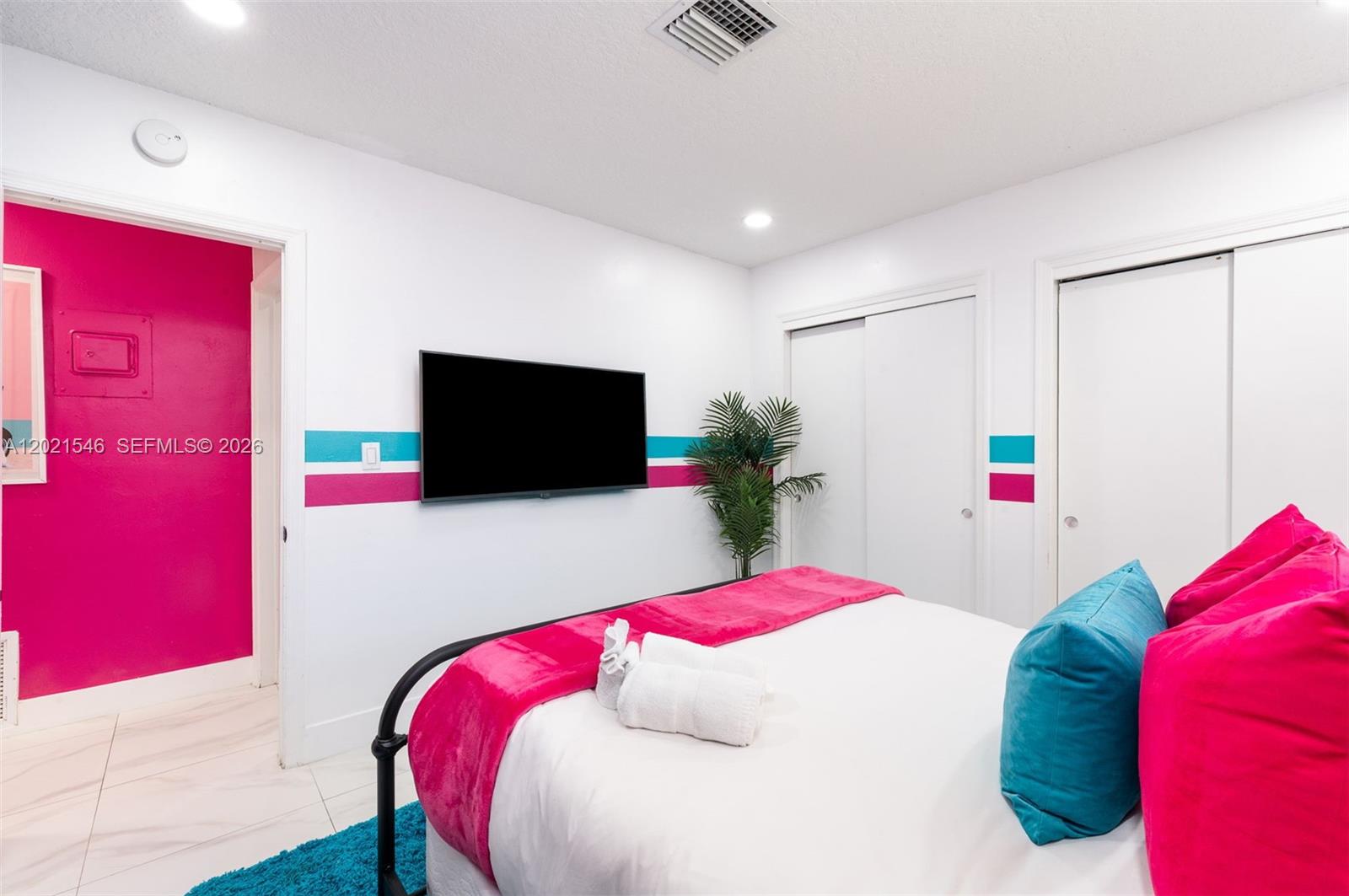 A bedroom features white walls with pink and teal stripes, a television, and pink bedding — 329 SE 12th Ave # 2, Pompano Beach FL 33060, POMPANO BEACH, FL
