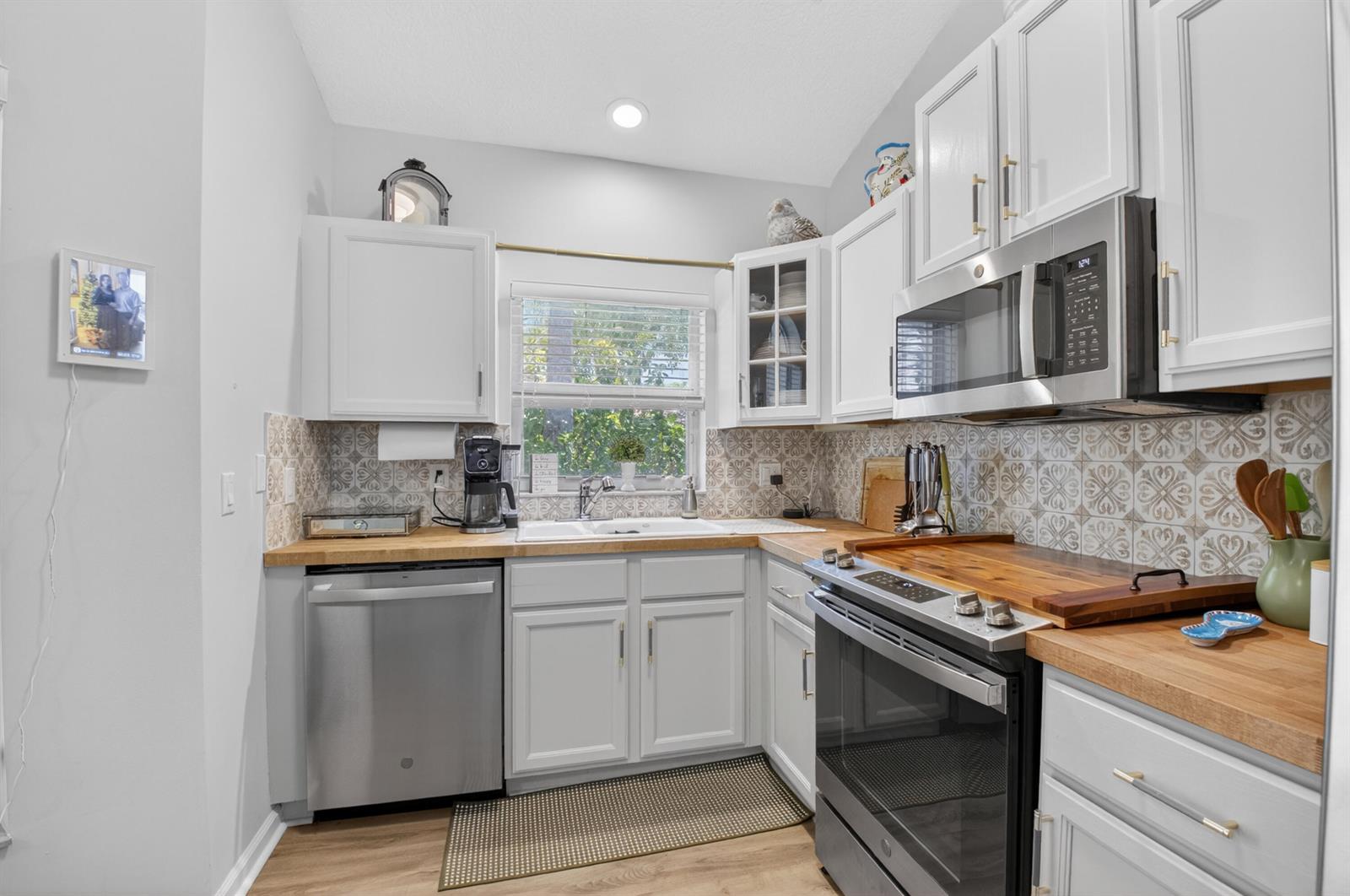 A kitchen features white cabinets, butcher block countertops, stainless steel appliances, and patterned tile backsplash — 8446 Vía Serena, Boca Raton FL 33433, BOCA RATON, FL