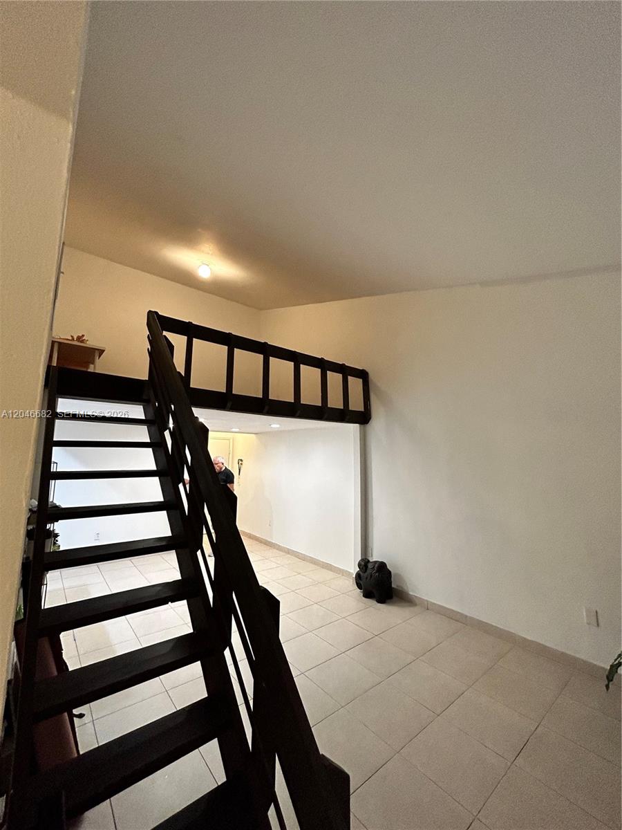A room with tiled floors, a dark wooden staircase, and an elevated loft area — 9421 Fontainebleau Blvd # 35, Miami FL 33172, MIAMI, FL