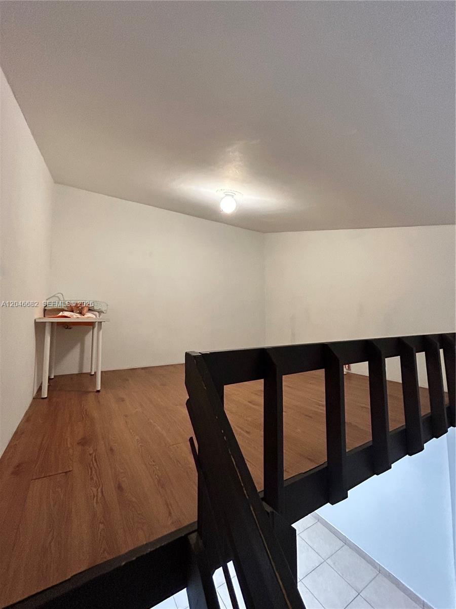 An interior view shows a loft area with wood-look flooring and a black wooden railing — 9421 Fontainebleau Blvd # 35, Miami FL 33172, MIAMI, FL