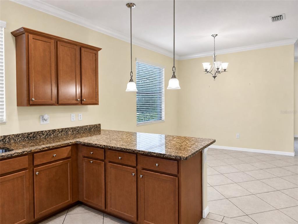 A kitchen with wood cabinets, granite countertops, and a dining area with a chandelier — 12889 RICHEZZA DRIVE, VENICE, FL