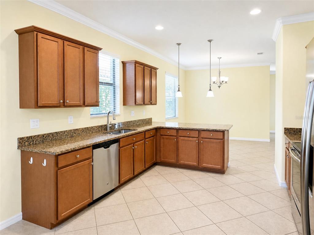 A kitchen with wood cabinets, granite countertops, stainless steel appliances, and light-colored tile flooring — 12889 RICHEZZA DRIVE, VENICE, FL