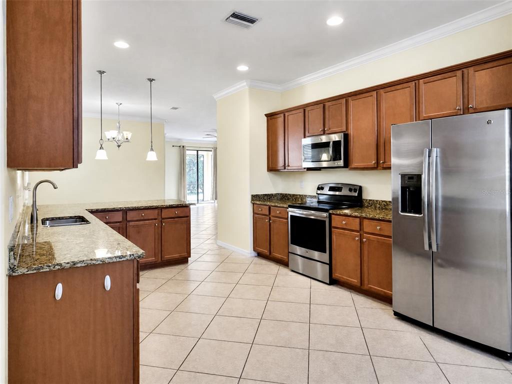 A kitchen with wood cabinets, granite countertops, stainless steel appliances, and tile flooring — 12889 RICHEZZA DRIVE, VENICE, FL