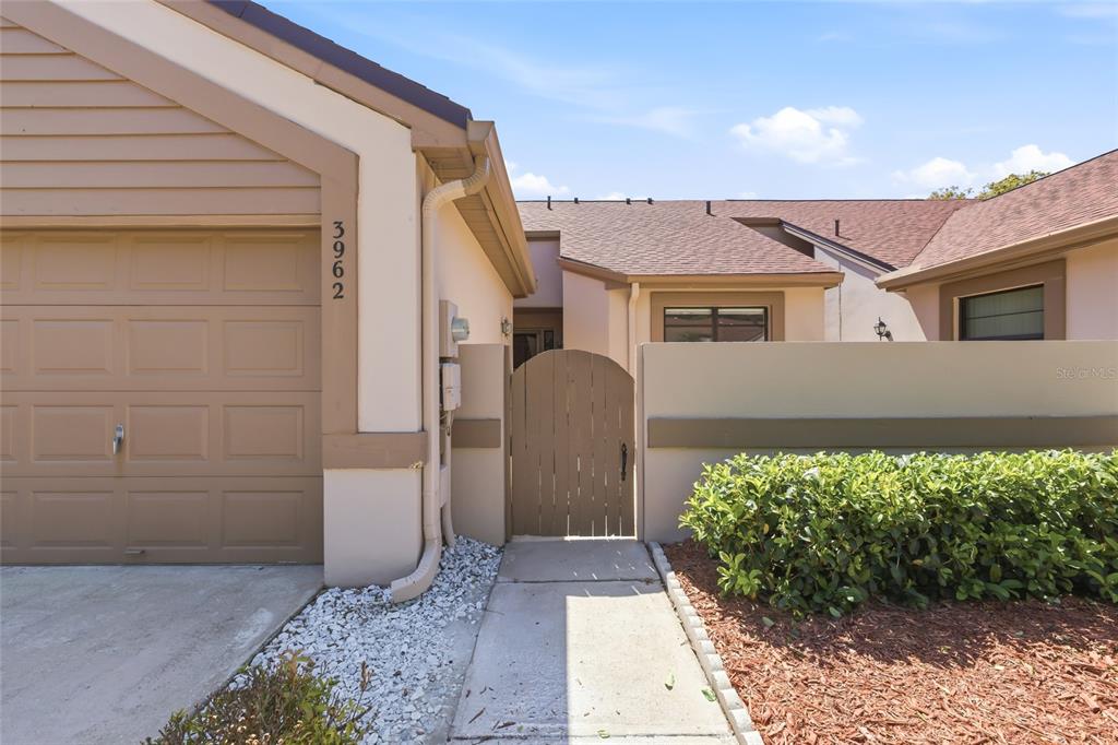 The exterior of a house features a garage, a wooden gate, and a concrete walkway — 3962 MERMOOR DRIVE, PALM HARBOR, FL