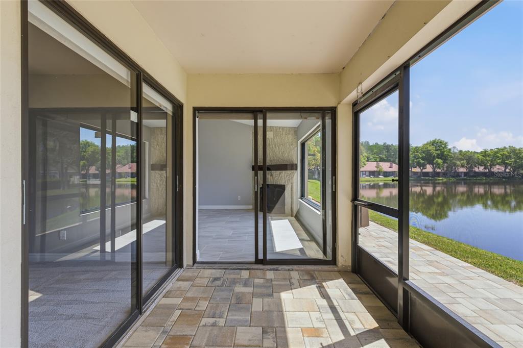 A covered patio with paver flooring overlooks a lake through screened-in walls — 3962 MERMOOR DRIVE, PALM HARBOR, FL
