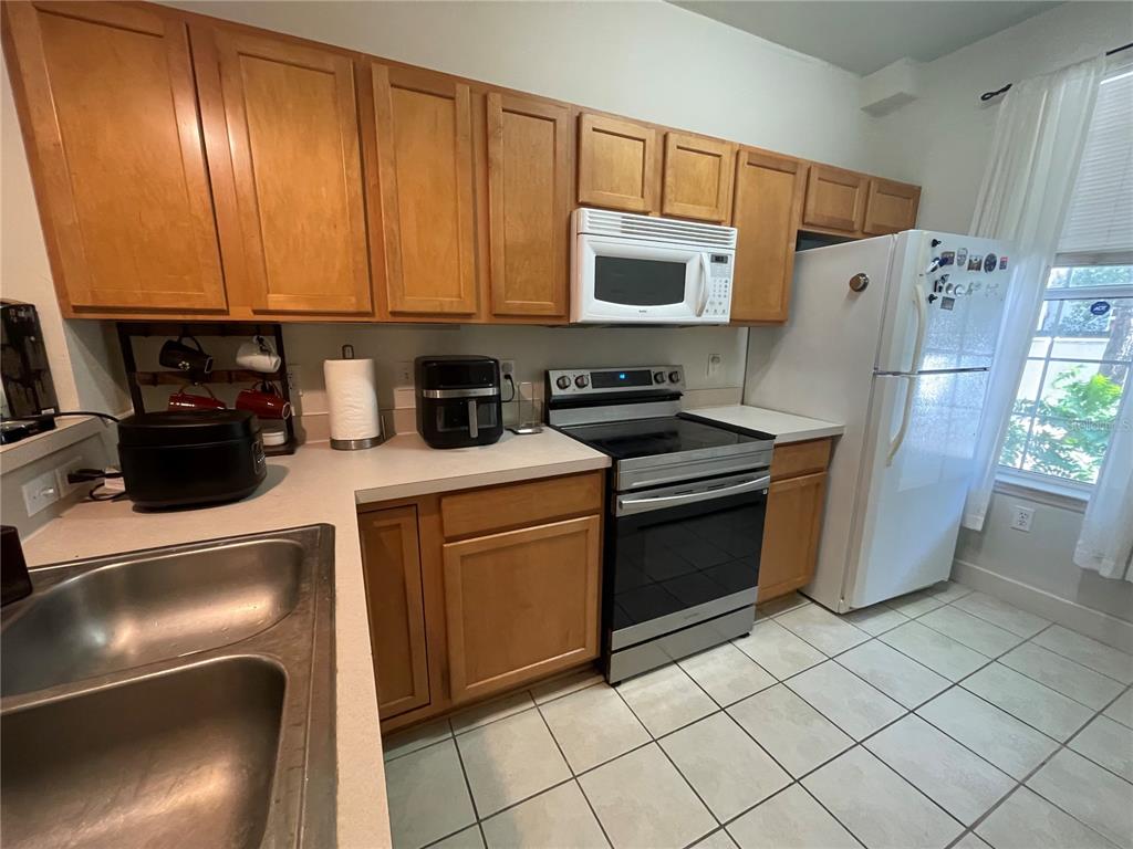 A kitchen features light wood cabinets, stainless steel appliances, a white refrigerator, and tiled flooring — 905 NW 21ST AVENUE UNIT 905, GAINESVILLE, FL