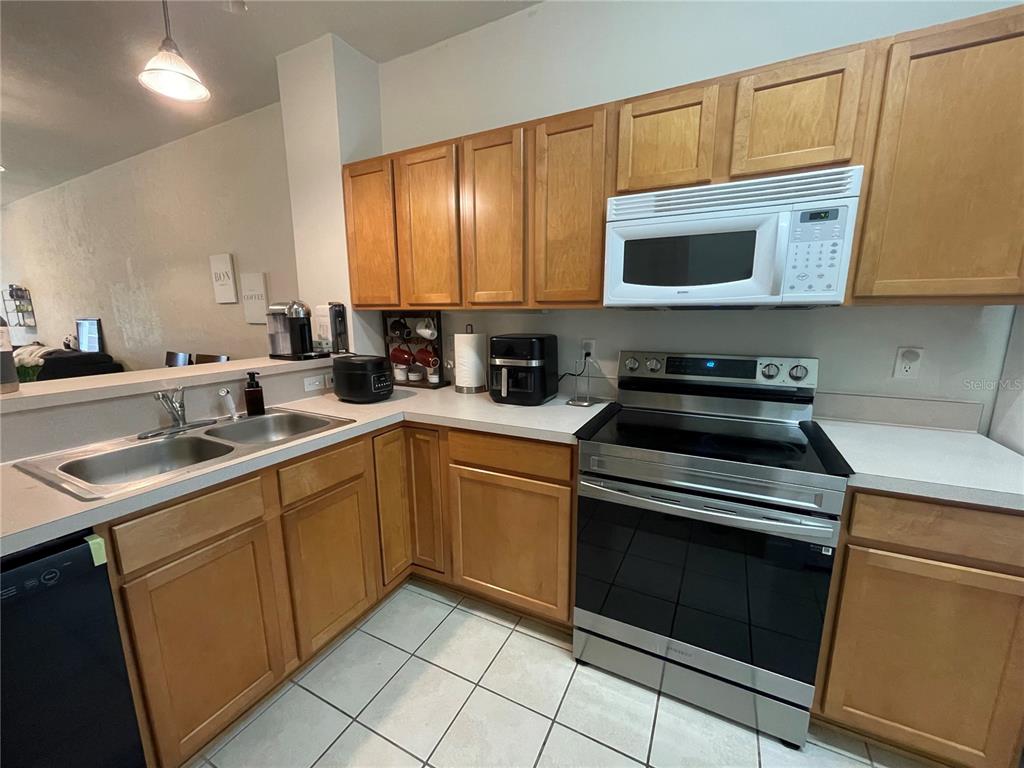 A kitchen features light wood cabinets, white countertops, stainless steel appliances, and tile flooring — 905 NW 21ST AVENUE UNIT 905, GAINESVILLE, FL