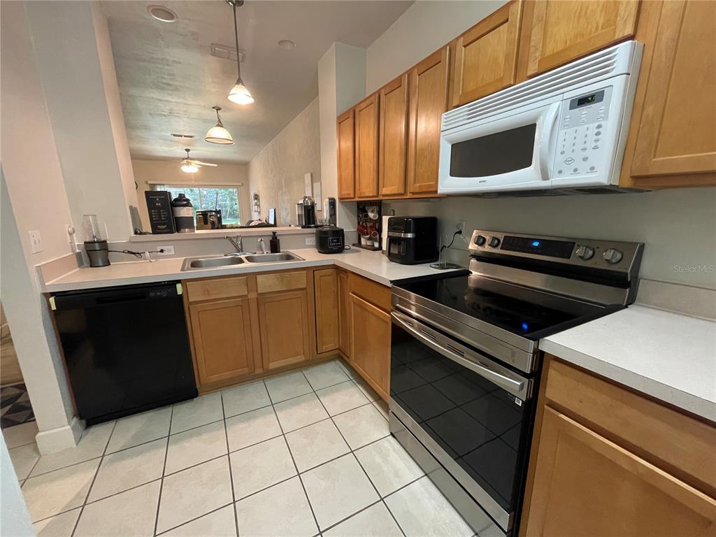 A kitchen features wood cabinets, white countertops, a black dishwasher, and a stainless steel stove — 905 NW 21ST AVENUE UNIT 905, GAINESVILLE, FL