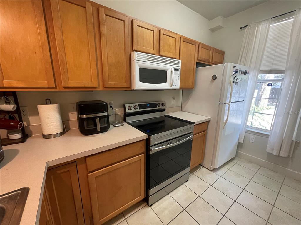 A kitchen with light wood cabinets, white appliances, a black stove, and tiled flooring — 905 NW 21ST AVENUE UNIT 905, GAINESVILLE, FL