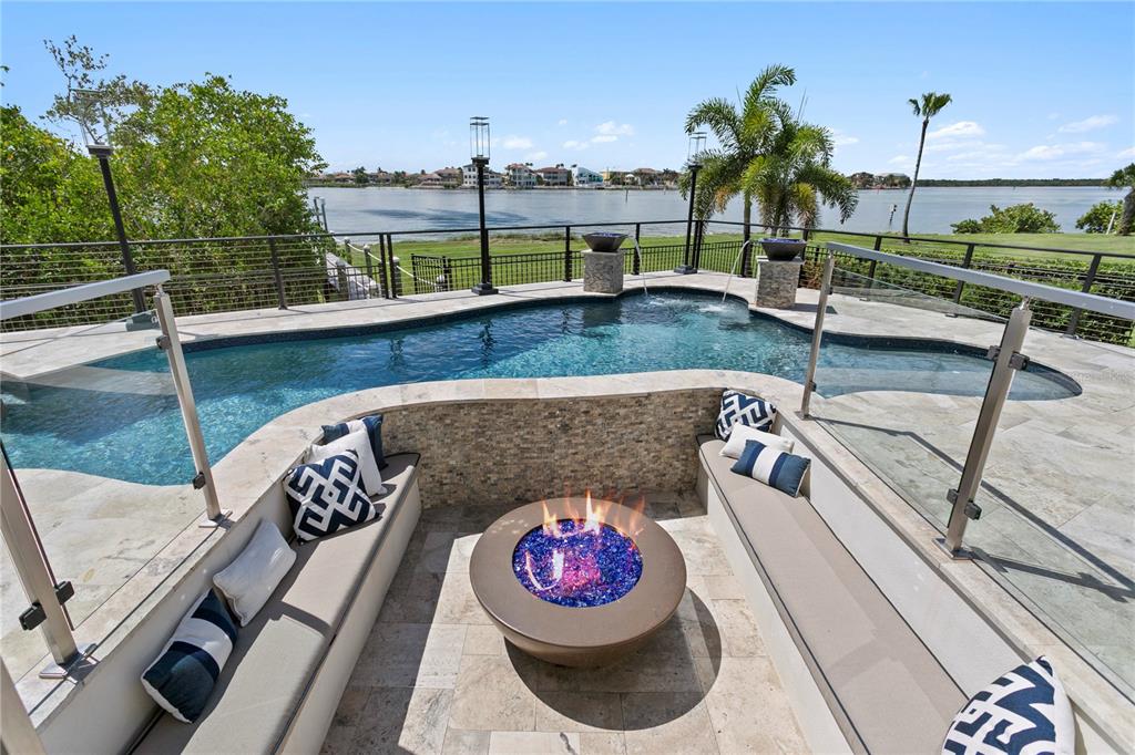 A sunken fire pit area with built-in seating overlooks a swimming pool and waterfront view — 1317 JUMANA LOOP, APOLLO BEACH, FL