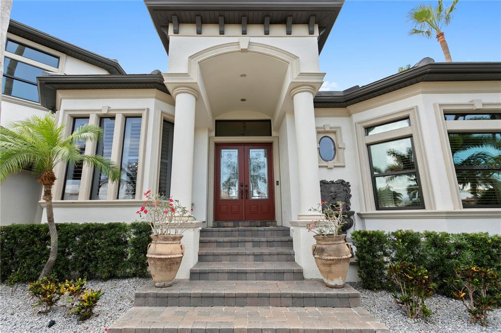 The front exterior of a house features a red double door, columns, and stone steps — 1317 JUMANA LOOP, APOLLO BEACH, FL