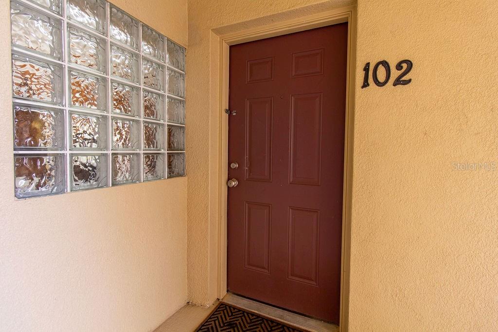 A red front door with the number 102 next to a glass block wall — 6445 CYPRESSDALE DRIVE UNIT 102, RIVERVIEW, FL