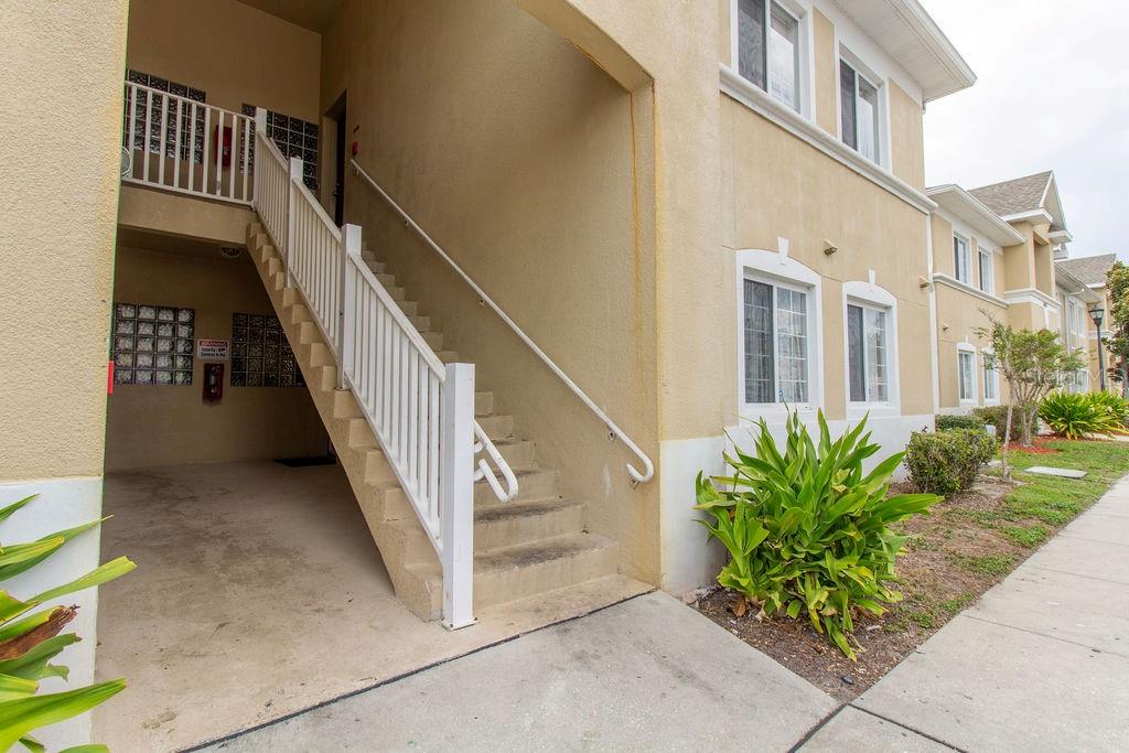 An exterior view of a tan apartment building featuring an outdoor staircase and mailboxes — 6445 CYPRESSDALE DRIVE UNIT 102, RIVERVIEW, FL