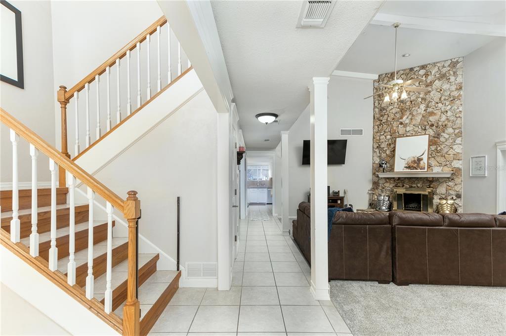 A view of a home interior featuring a staircase, tiled hallway, and a stone fireplace — 932 PELICAN BAY DRIVE, DAYTONA BEACH, FL
