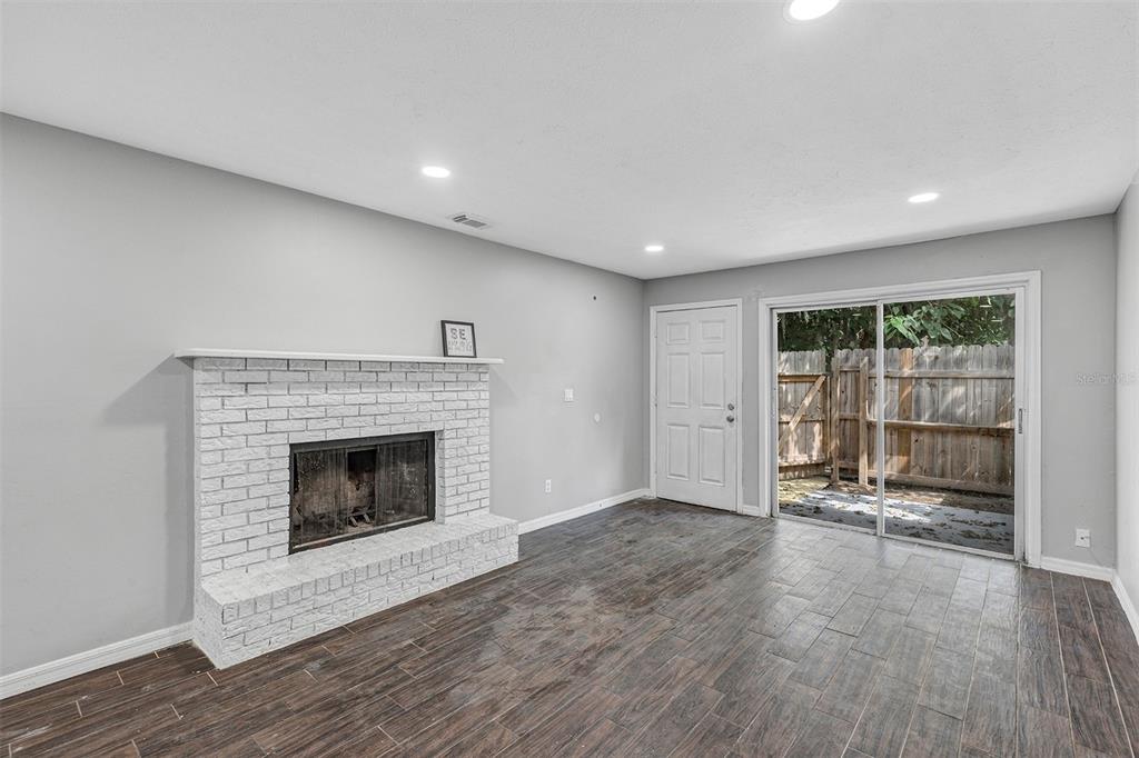A living room features a white brick fireplace, wood-look tile flooring, and sliding glass doors — 3990 SE 17TH CT UNIT B, OCALA, FL
