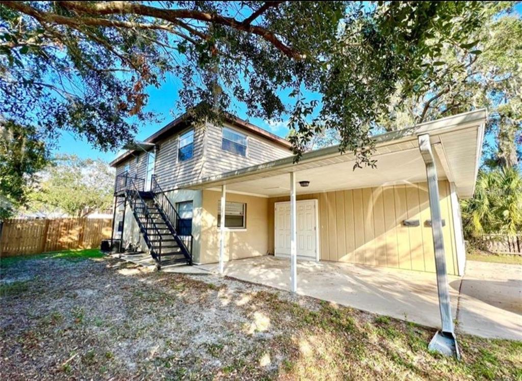 A two-story house exterior featuring a metal staircase, a concrete carport, and tan siding — 209 AVENUE B SE, WINTER HAVEN, FL