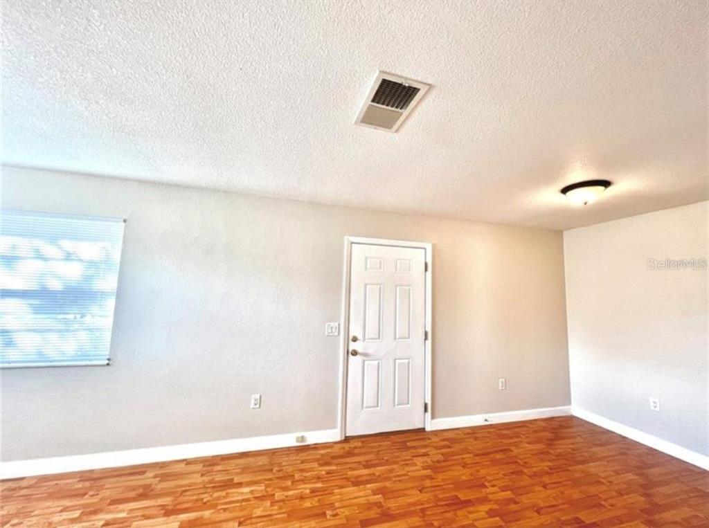 An empty room features light-colored walls, wood-look flooring, a white door, and a ceiling vent — 209 AVENUE B SE, WINTER HAVEN, FL