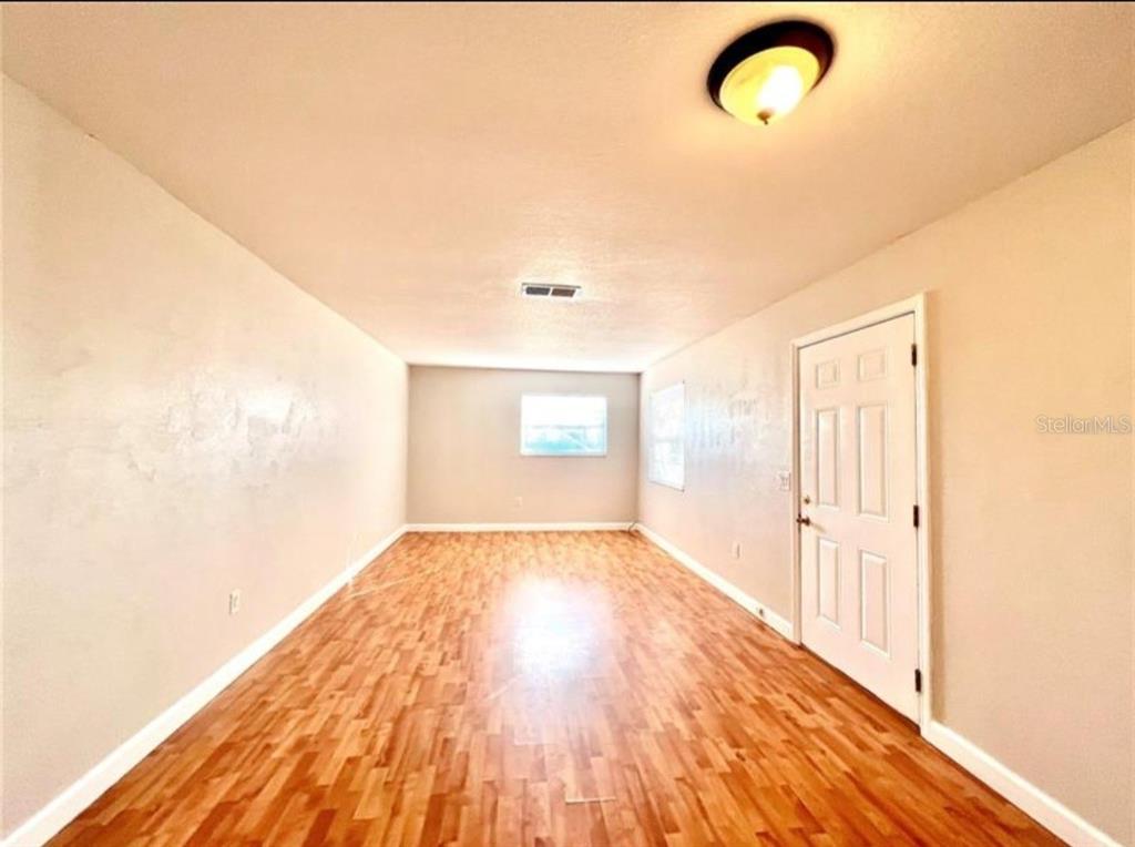 An empty room with light wood-look flooring, beige walls, a white door, and ceiling lighting — 209 AVENUE B SE, WINTER HAVEN, FL