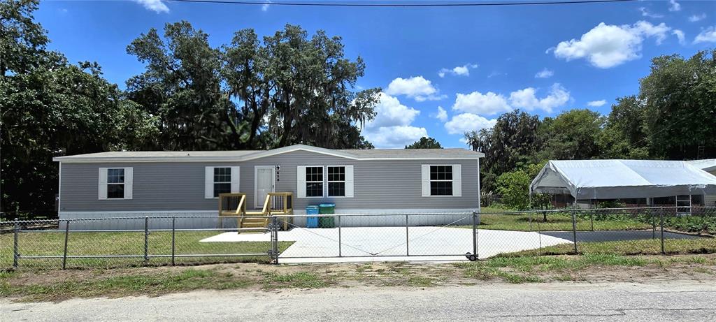 A single-story manufactured home with light gray siding, a concrete driveway, and a chain-link fence — 659 ALPINE STREET, MASCOTTE, FL