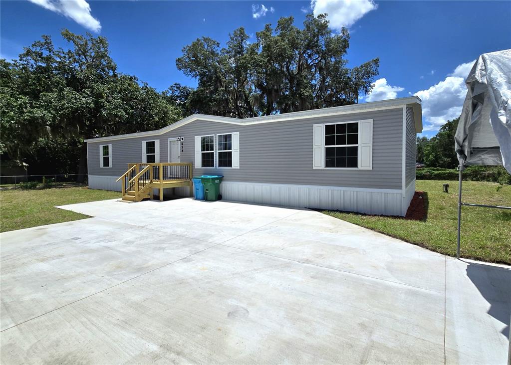 A gray manufactured home exterior features a wooden front porch and two plastic trash bins — 659 ALPINE STREET, MASCOTTE, FL