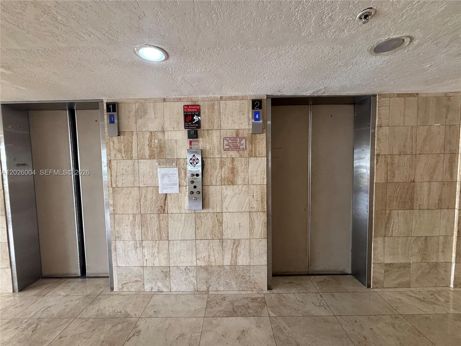 Two elevators with beige tiled walls and floors are located in a building hallway — 1800 NW 24th Ave # 314, Miami FL 33125, MIAMI, FL