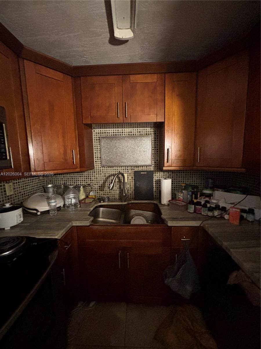 A kitchen features wooden cabinets, a double sink, and a mosaic tile backsplash — 1800 NW 24th Ave # 314, Miami FL 33125, MIAMI, FL