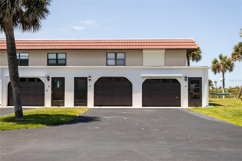 The exterior of a two-story townhouse complex features three garage doors and matching entry doors — 23 OCEAN PALM VILLA DRIVE N, FLAGLER BEACH, FL